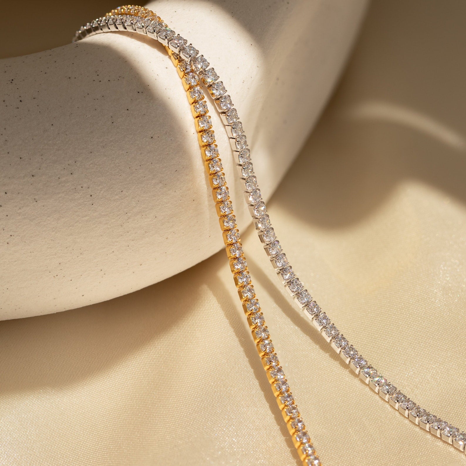 A Classic Diamond Tennis Bracelet in White Gold elegantly draped over a textured cream ceramic bowl—an exquisite display of timeless diamond jewelry.