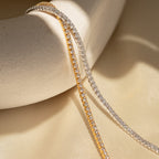 The Dainty Diamond Tennis Necklace & Bracelet Set in 18K Gold gleams atop a cream ceramic bowl and fabric—an elegant anniversary jewelry choice.