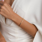 Woman in a white dress wears the Blue Diamond Tennis Bracelet, a minimalist gold accessory, while holding a cup near her chest.
