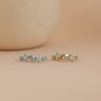 Side-by-side display of both gold and silver Aquamarine Diamond Huggies on a soft peach backdrop.