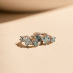 Close-up view of the silver Aquamarine Diamond Huggies lying on a peach-toned surface, with their gemstones shimmering under light.