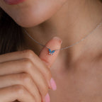 A woman displays the Blue Opal Butterfly Necklace, featuring a delicate blue opal butterfly pendant near her neck, highlighting its elegant design.