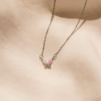 The Pink Opal Butterfly Necklace features a silver chain and an iridescent butterfly pendant, beautifully displayed on a soft beige fabric background.