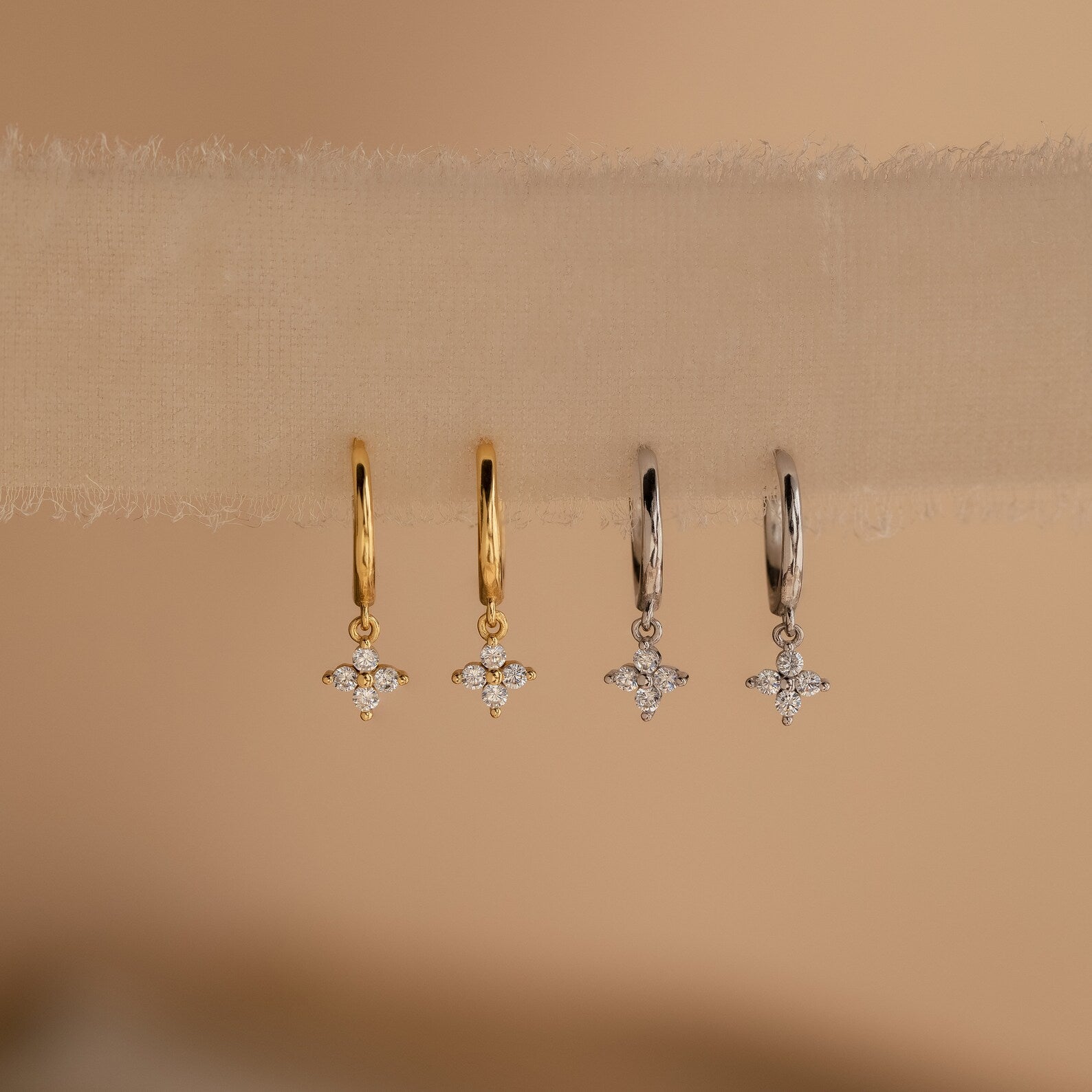 Four Diamond Flower Huggie earrings (two gold, two silver) neatly aligned on a soft tulle ribbon