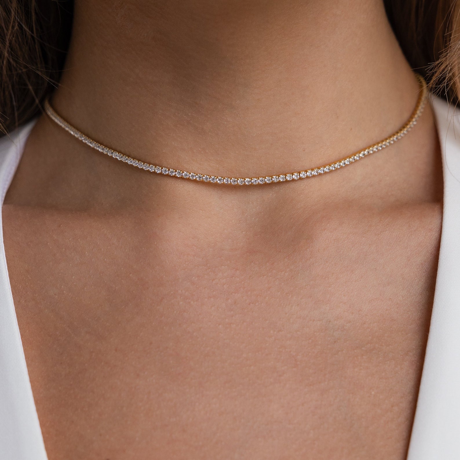 Close-up of a woman's neck wearing the Dainty Diamond Tennis Necklace & Bracelet Set in 18K Gold with a white V-neck top—a refined pick for anniversary jewelry.