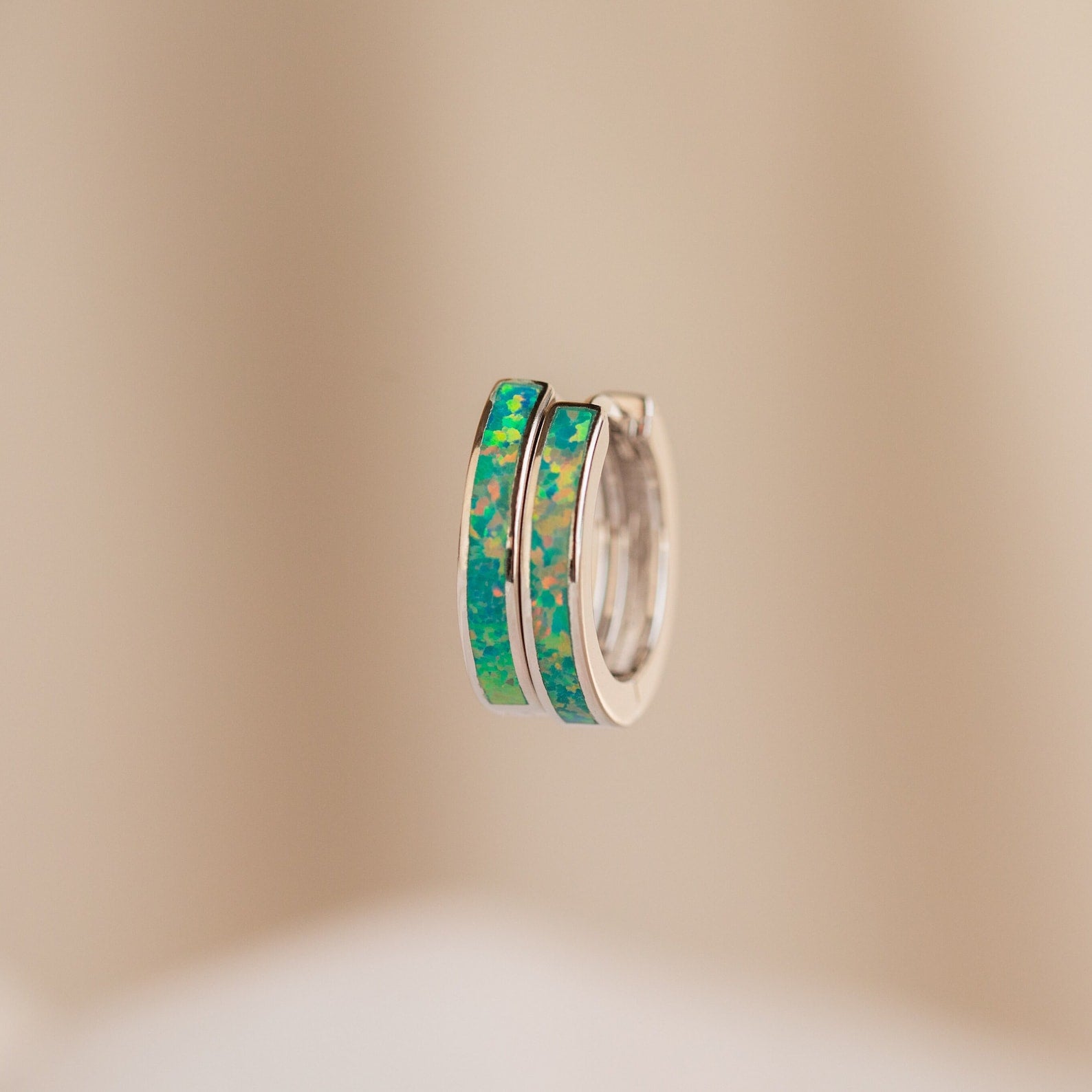 Close-up of two silver Green Opal Inlay Hoops, featuring vibrant blue-green opal inlay, displayed on a neutral beige background.
