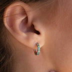 Close-up of a person’s ear adorned with small hoop earrings featuring a blue-green inlay, similar to the elegant Green Opal Inlay Hoops.