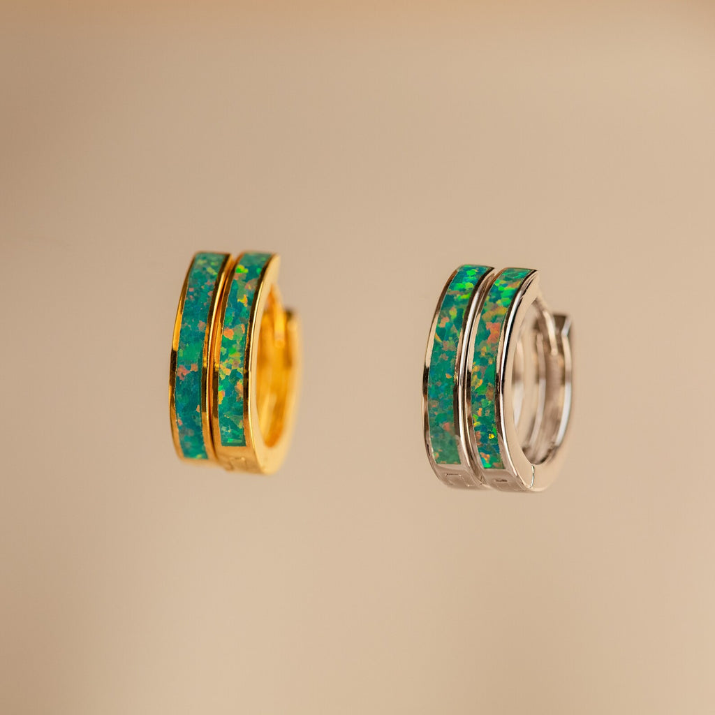Two small hoop earrings, one gold and one silver, each with a green and blue marbled opal inlay, are shown on a beige background—perfect as Green Opal Inlay Hoops.