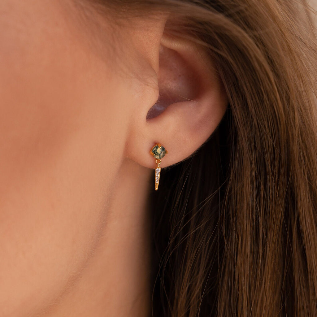 Close-up of a woman's ear wearing Agate Diamond Drop Earrings: elegant gold earrings featuring green gemstones and small hanging charms.