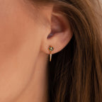Close-up of a woman's ear wearing Agate Diamond Drop Earrings: elegant gold earrings featuring green gemstones and small hanging charms.