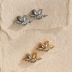 Two pairs of Aquamarine Marquise Studs—one in silver, one in gold—are displayed on textured beige paper. These sparkling gemstone earrings are perfect as bridesmaids gifts and add a touch of elegance with their floral design.