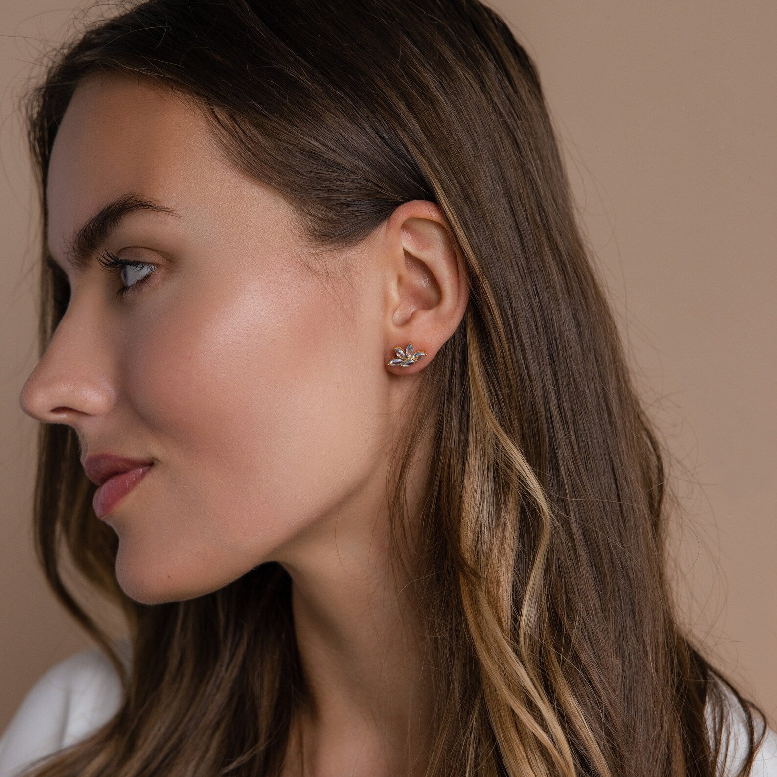 Woman with long brown hair wears Aquamarine Marquise Studs, delicate earrings that make an elegant bridesmaid gift, against a beige background.