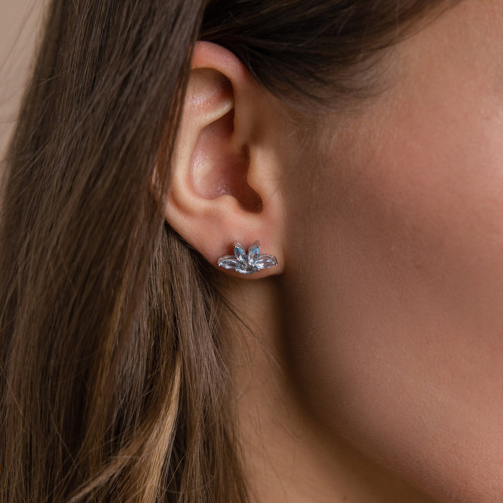 Close-up of a woman’s ear wearing Aquamarine Marquise Studs—silver earrings with a leaf-inspired design and sparkling aquamarine stones; perfect as floral earrings or an elegant bridesmaids gift.