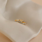 Two gold rings with small blue gemstones rest on cream-colored fabric—perfect for pairing with your Aquamarine Pave Huggies for an elegant ear stack.