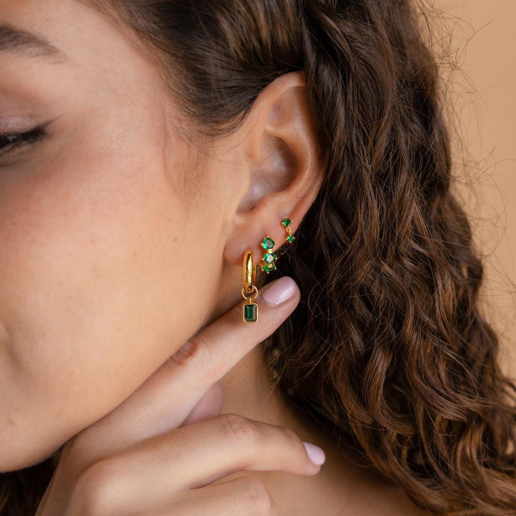 Close-up of a woman's ear adorned with Dangling Emerald Birthstone Hoops, her finger gently touching her chin.