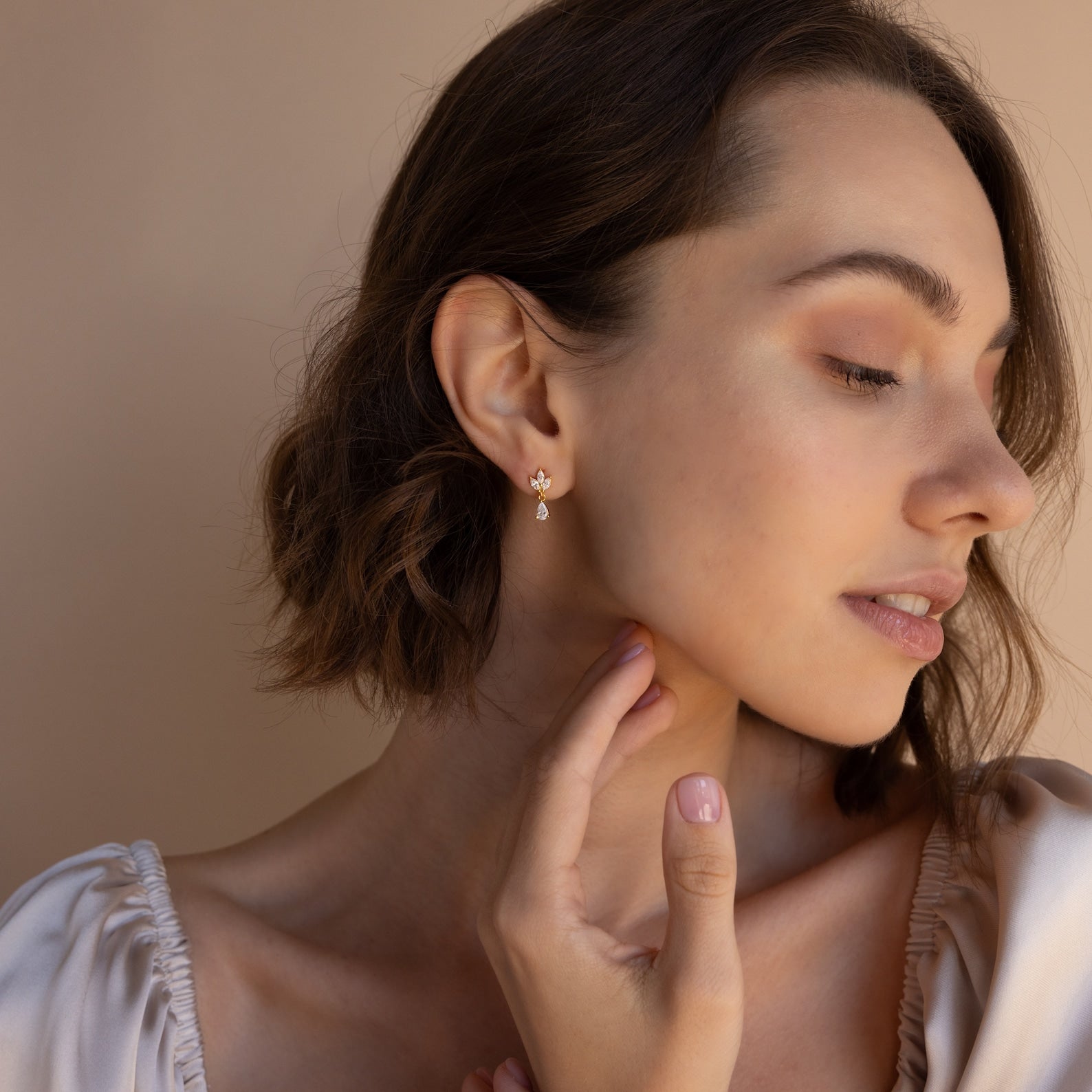 A woman with short brown hair, wearing Marquise Diamond Drop Studs, gently touches her neck while looking to the side.