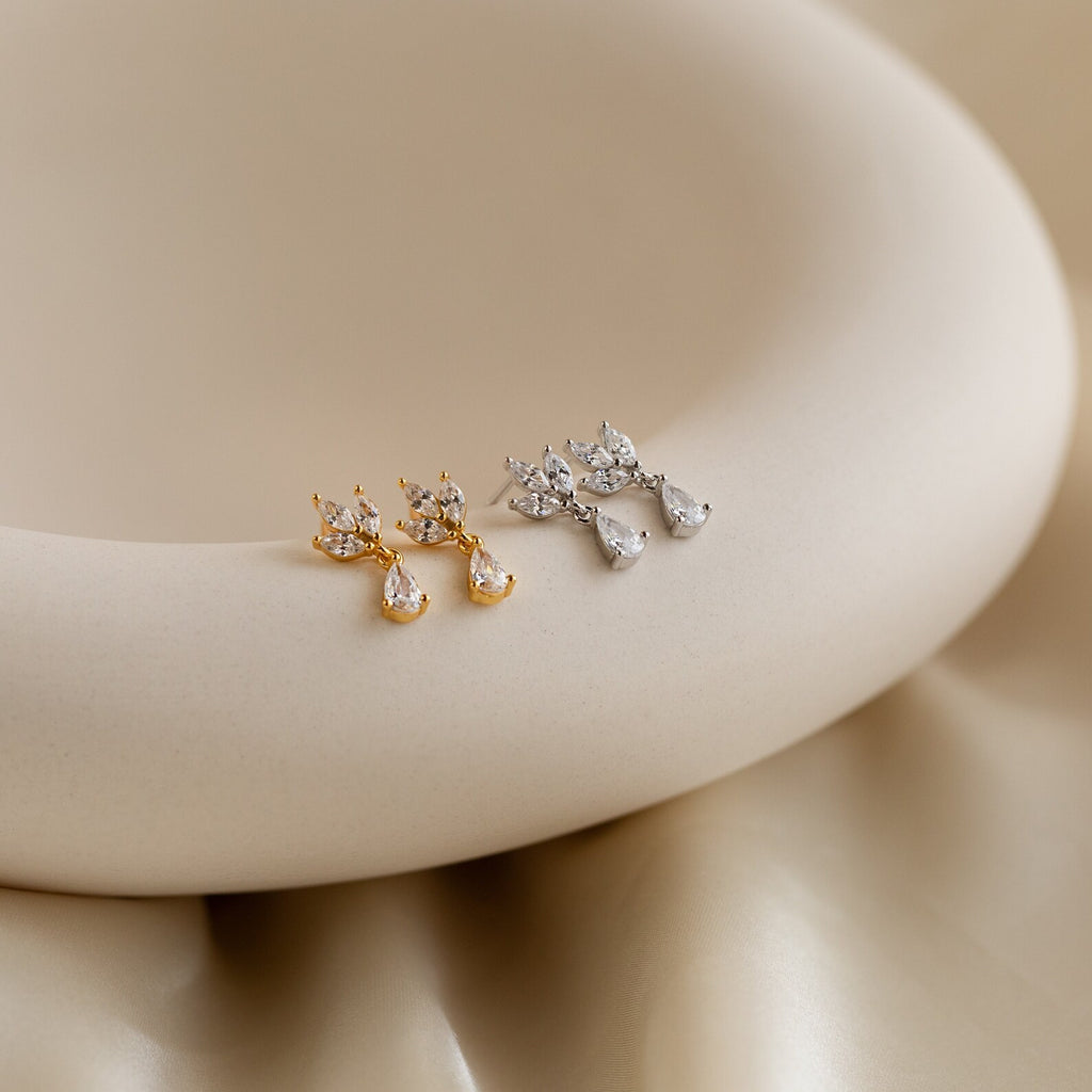 The Marquise Diamond Drop Studs—one gold pair and one silver pair, inspired by elegant Marquise-Cut Diamonds—are displayed on a smooth, cream-colored surface.
