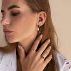 A woman with long brown hair wears a white top, gold rings, and Emerald Pearl Drop Earrings.