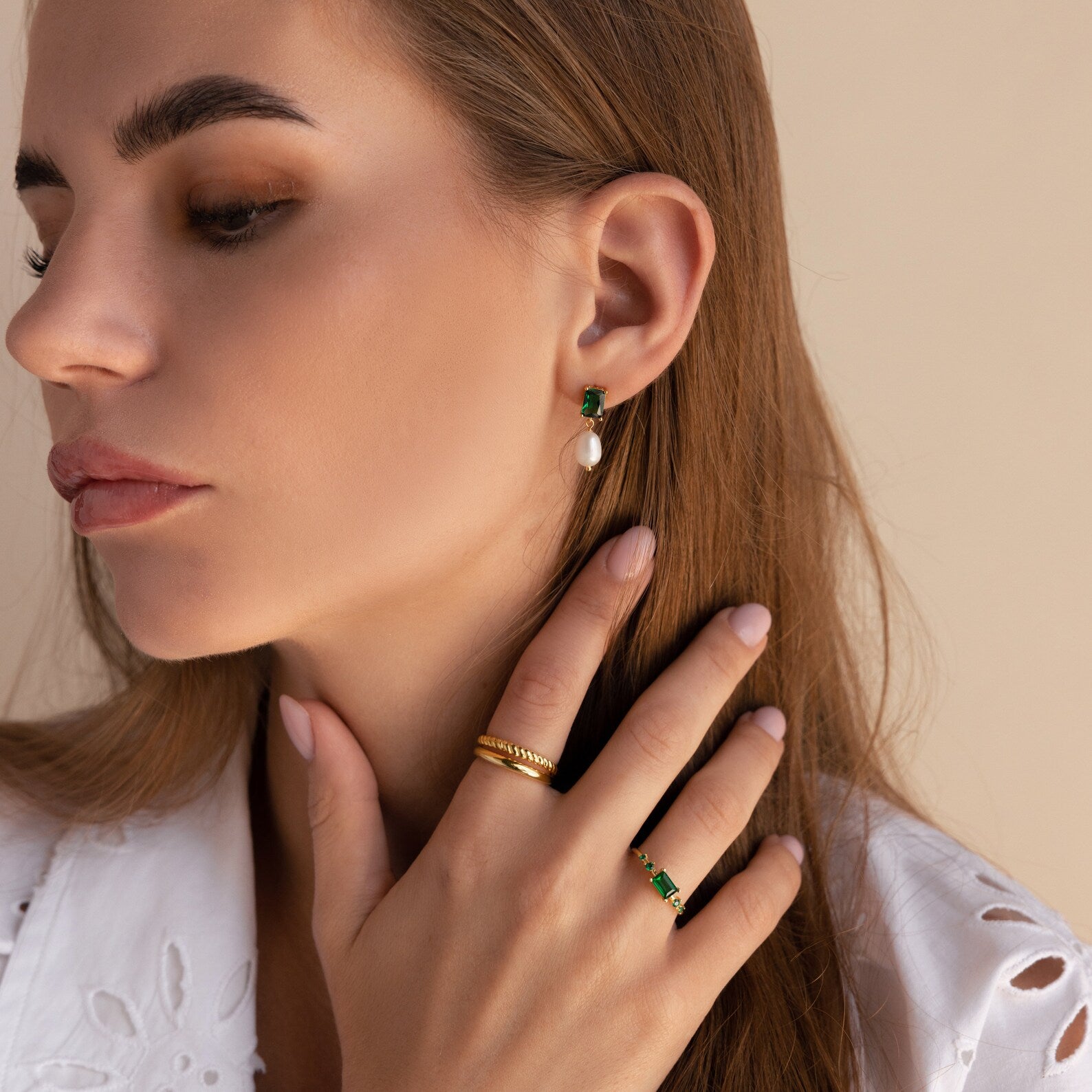 A woman with long brown hair wears a white top, gold rings, and Emerald Pearl Drop Earrings.