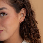Woman with curly brown hair wearing the Triple Diamond Studs Set, along with gold and pearl stacking earrings.