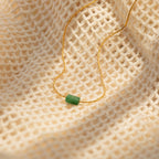 Minimalist gold necklace with a small horizontal jade bar pendant, displayed on a textured cream fabric background.