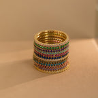 A stack of Eternity Birthstone Rings is set with colorful gemstones and arranged on a beige surface under warm lighting—an elegant, customizable ring and the perfect Christmas gift.