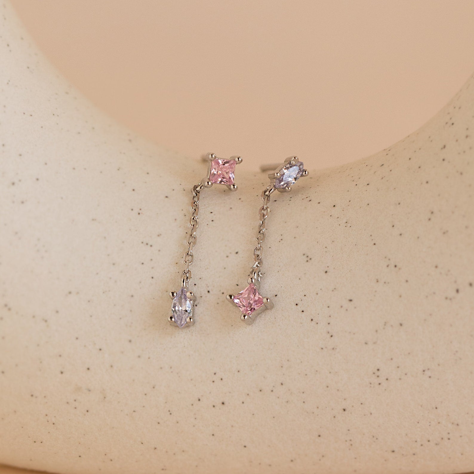 Mixed Crystal Drop Earrings feature two delicate dangling chain studs with pink and clear gemstones, displayed on a speckled beige surface—perfect minimalist earrings for an elegant look.