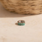 A silver ring with two rows of turquoise stones sits on a light surface near a woven basket—the perfect complement to your Garden Green Opal Huggies.