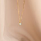 Tiny Opal Heart Necklace with a delicate, light blue opal heart-shaped charm shown on a soft beige background.