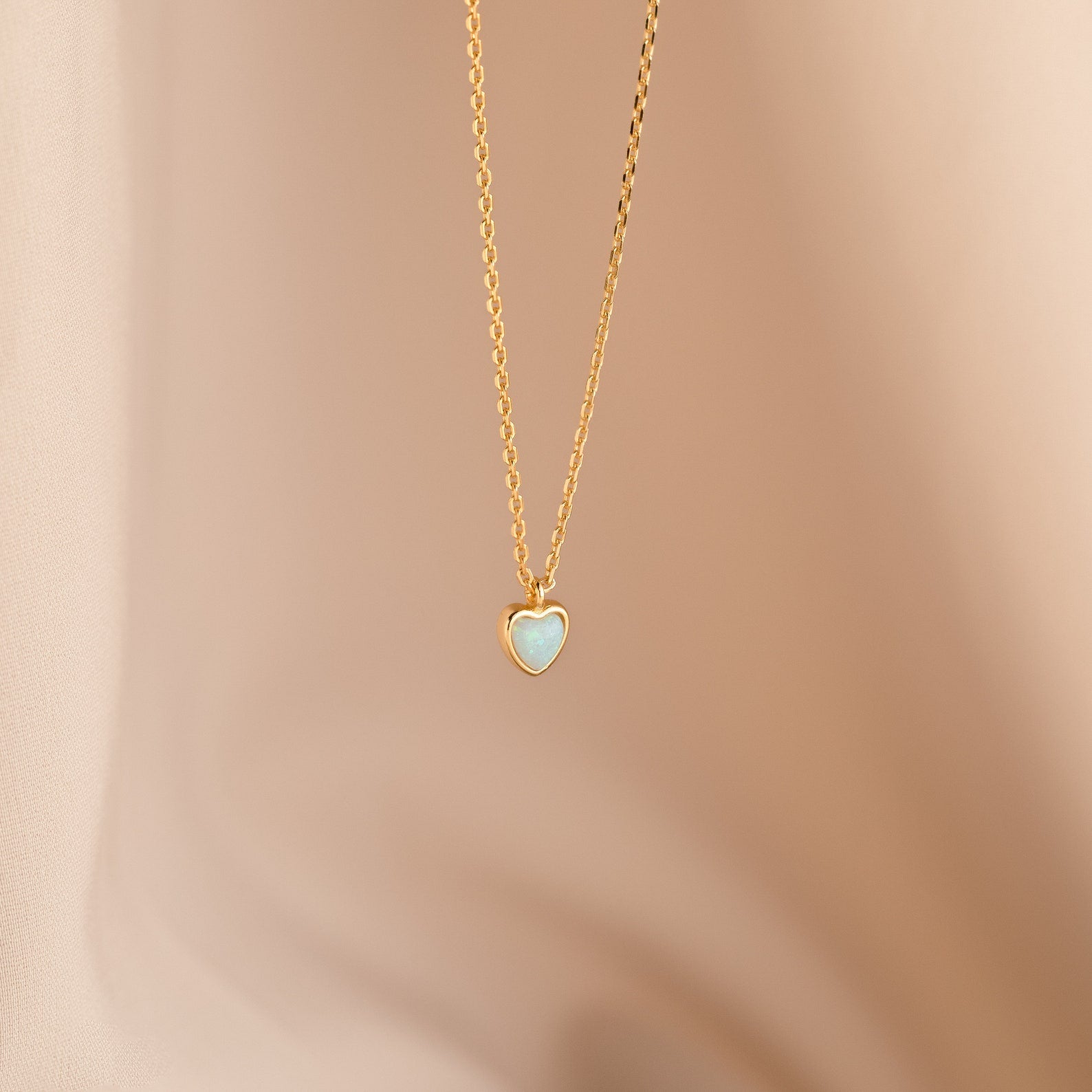 Tiny Opal Heart Necklace with a delicate, light blue opal heart-shaped charm shown on a soft beige background.