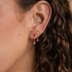 Close-up of a woman's ear with curly brown hair wearing Mixed Pink Drop Earrings—gold featuring pink and purple gemstones.