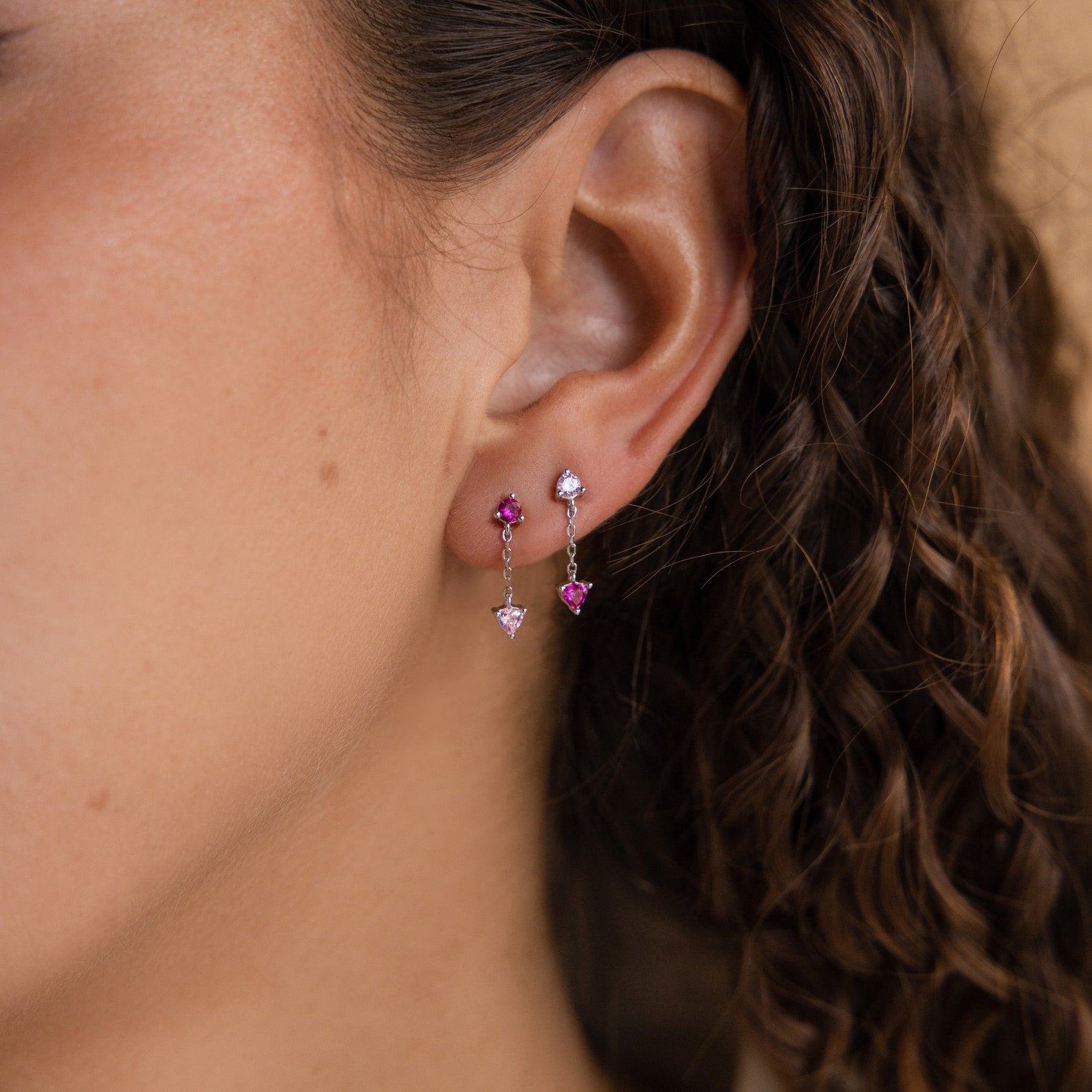 Close-up of a woman's ear with curly brown hair, wearing Mixed Pink Drop Earrings—romantic mismatched earrings featuring dazzling pink gemstones.