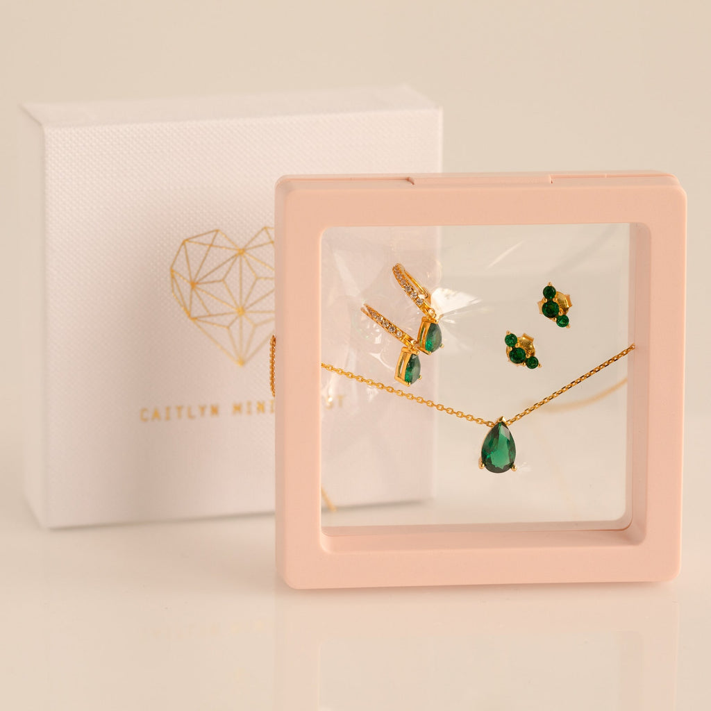 Gold and green gemstone necklace and earring set in a pink display case with a Caitlyn Minimalist box—perfect as a Birthstone Mystery Box or for a personalized surprise gift.
