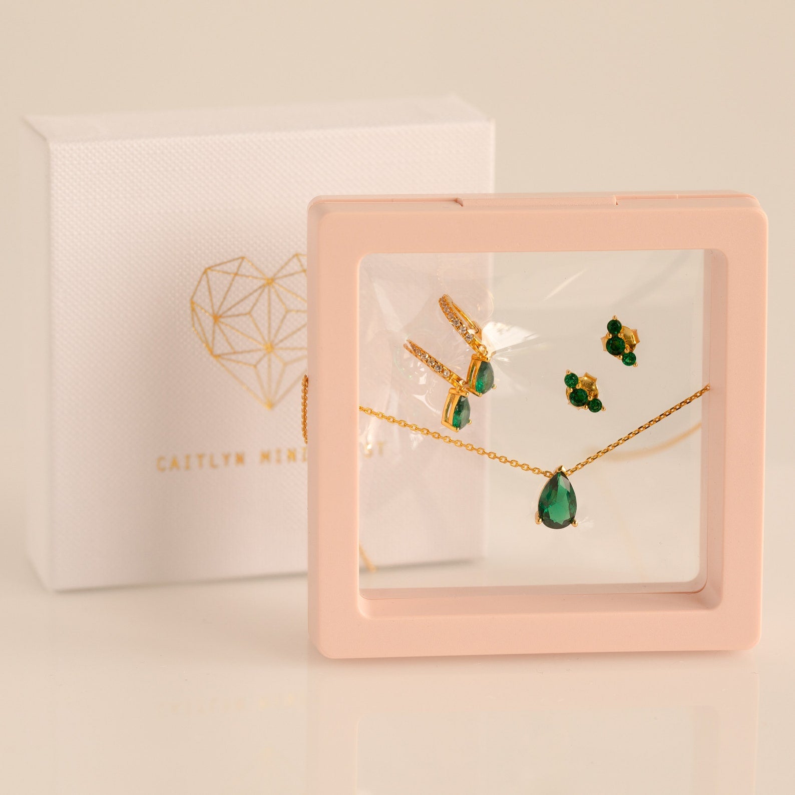 Gold and green gemstone necklace and earring set in a pink display case with a Caitlyn Minimalist box—perfect as a Birthstone Mystery Box or for a personalized surprise gift.