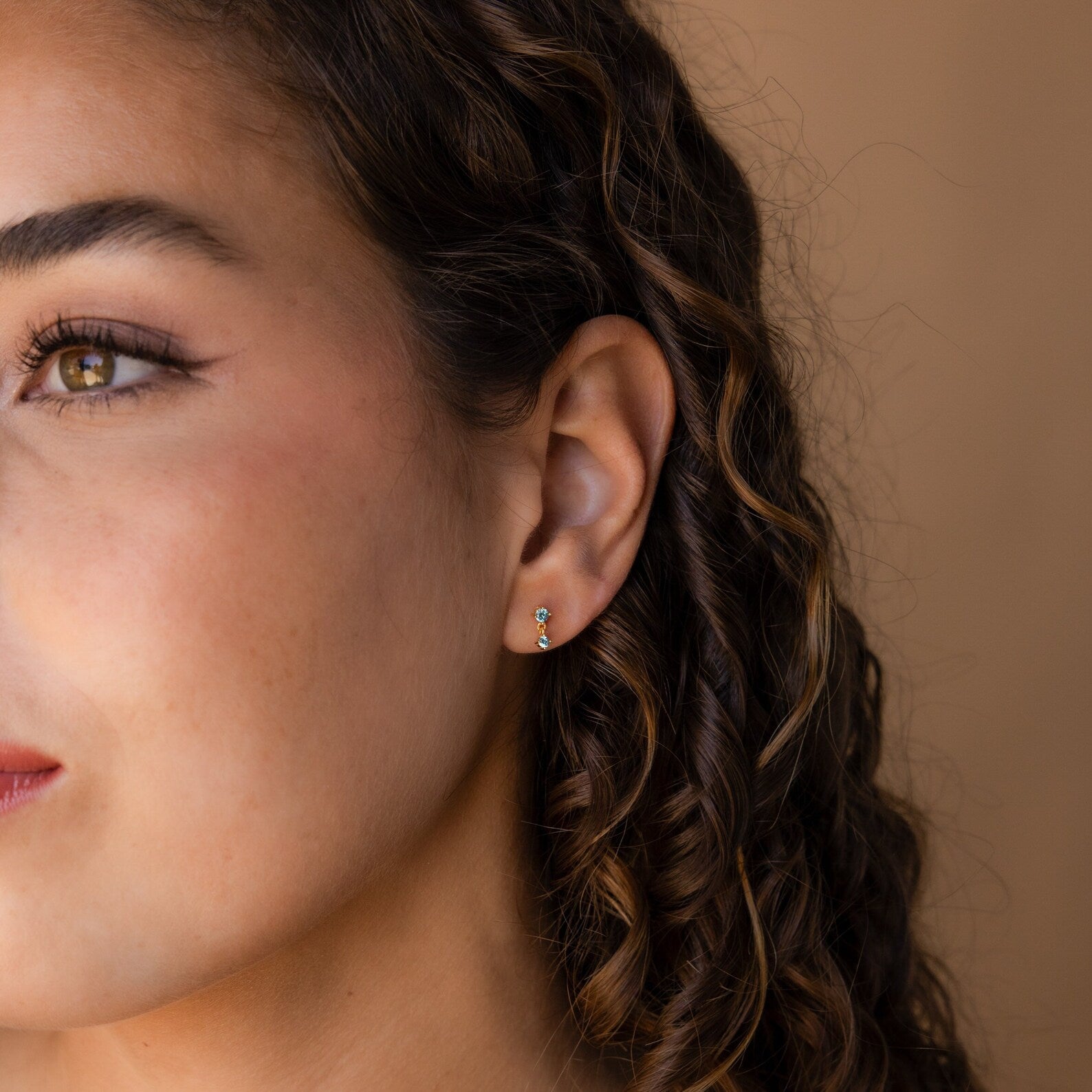Close-up of a woman with curly hair wearing the Birthstone Drop Studs against a neutral background.