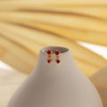 Ruby Birthstone Drop Studs featuring red gemstones displayed on a smooth white vase against a soft beige background.