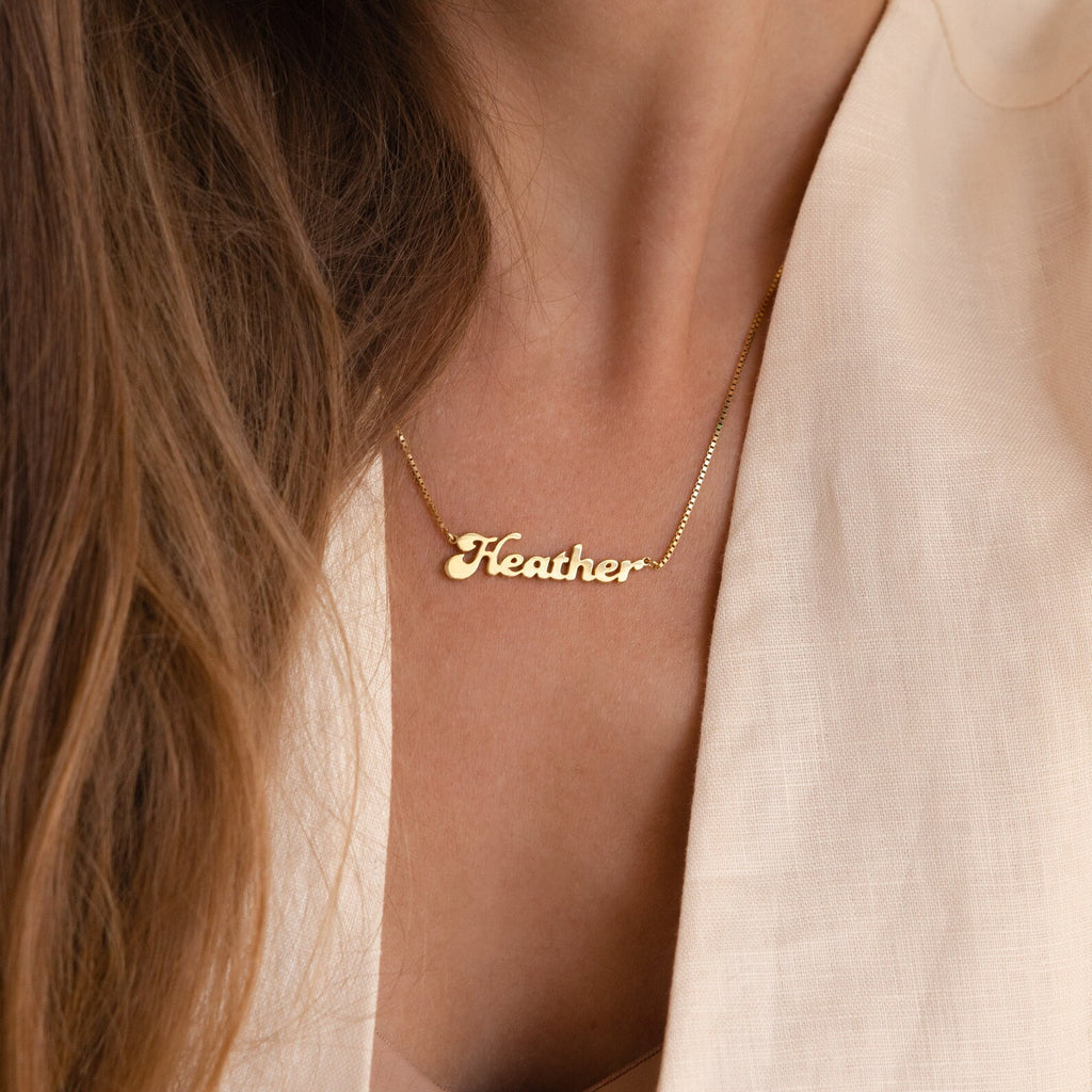 A person in a light beige top wears the Groovy Name Necklace in Box Chain, highlighting the elegance of custom jewelry.