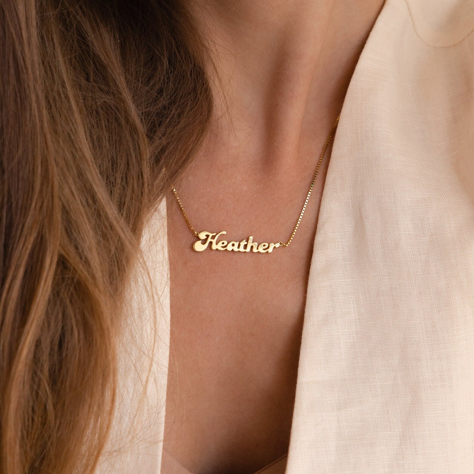A person in a light beige top wears the Groovy Name Necklace in Box Chain, highlighting the elegance of custom jewelry.