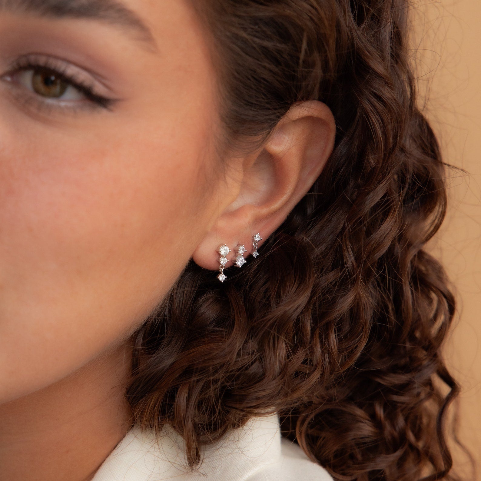 Close-up of a woman's ear adorned with the Triple Diamond Studs Set and small sparkling gemstone earrings.