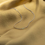 The Dainty Aventurine Bar Necklace, featuring a slim silver chain and small aventurine bar, rests gently on soft gold fabric.