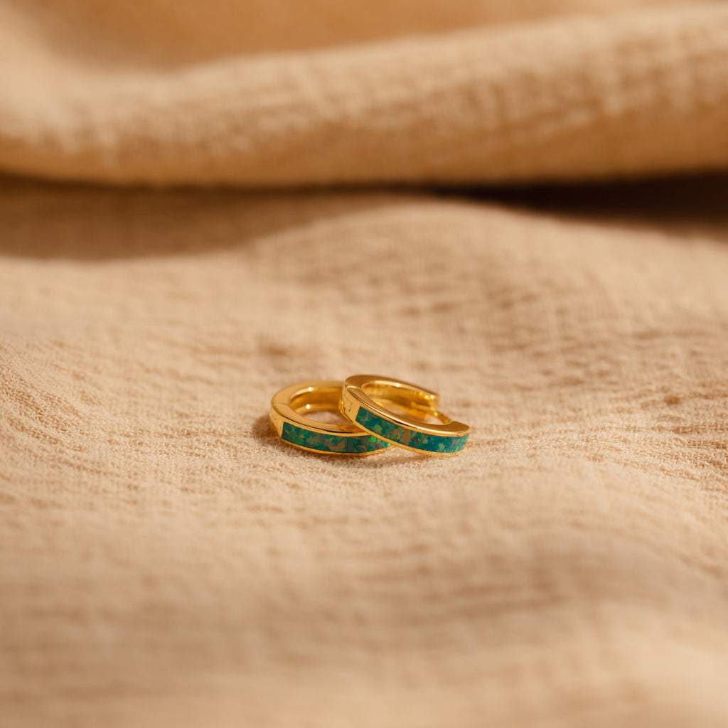 Two delicate Green Opal Inlay Huggies rest on beige textured fabric, offering a subtle pop of color to elevate your everyday style.