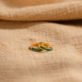 Two delicate Green Opal Inlay Huggies rest on beige textured fabric, offering a subtle pop of color to elevate your everyday style.