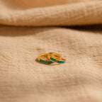 Two delicate Green Opal Inlay Huggies rest on beige textured fabric, offering a subtle pop of color to elevate your everyday style.