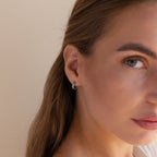 Close-up of a woman with light brown hair, wearing Green Opal Inlay Huggies and looking towards the camera.