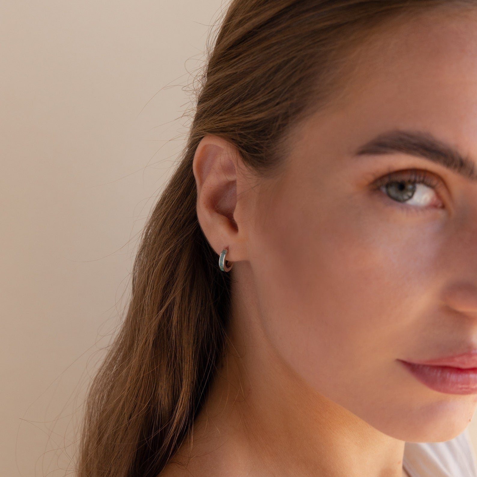 Close-up of a woman with light brown hair, wearing Green Opal Inlay Huggies and looking towards the camera.