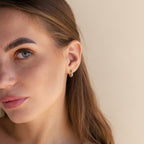 Close-up of a woman with long brown hair wearing Green Opal Inlay Huggies against a neutral background.