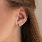 Close-up of a woman's ear with Green Opal Inlay Huggies; her brown hair is tucked behind her ear, showcasing the dainty earrings.