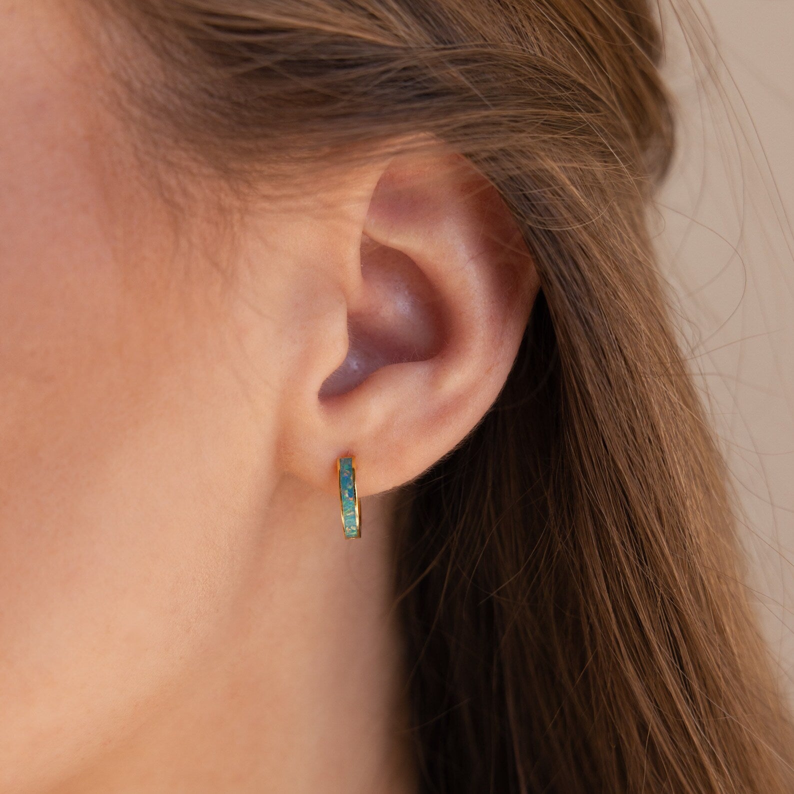 Close-up of a woman's ear with Green Opal Inlay Huggies; her brown hair is tucked behind her ear, showcasing the dainty earrings.