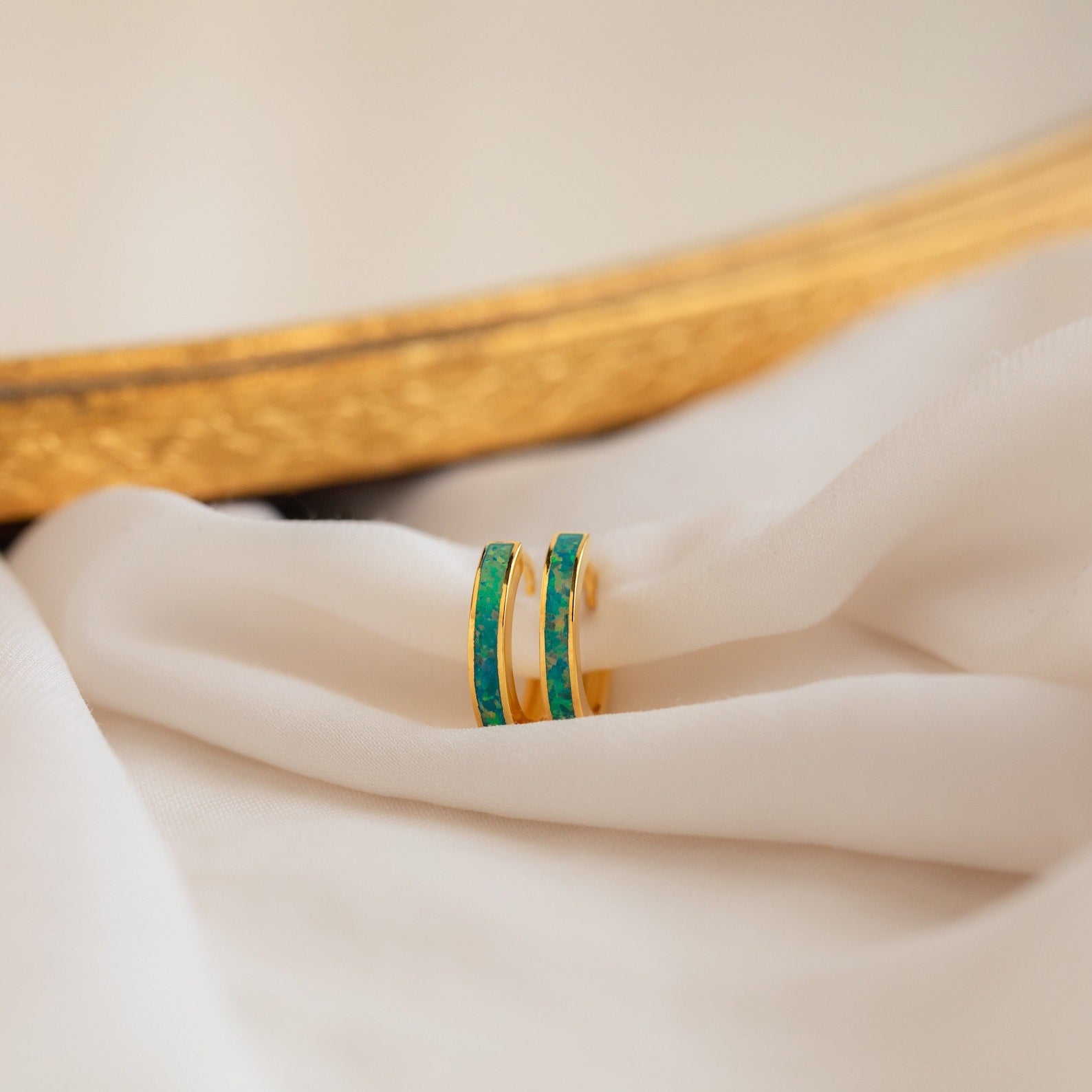 A pair of Green Opal Inlay Hoops featuring vibrant green stones, displayed on a white cloth.