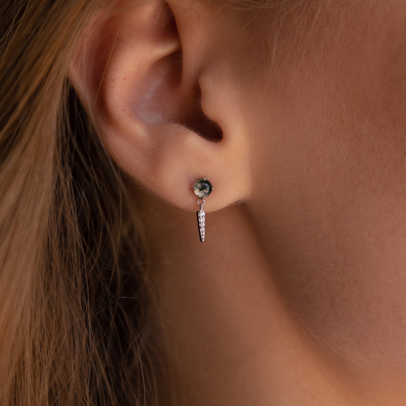 Close-up of a woman's ear adorned with Agate Diamond Drop Earrings—a small stud paired with a dangling dagger-shaped charm, exuding elegance.